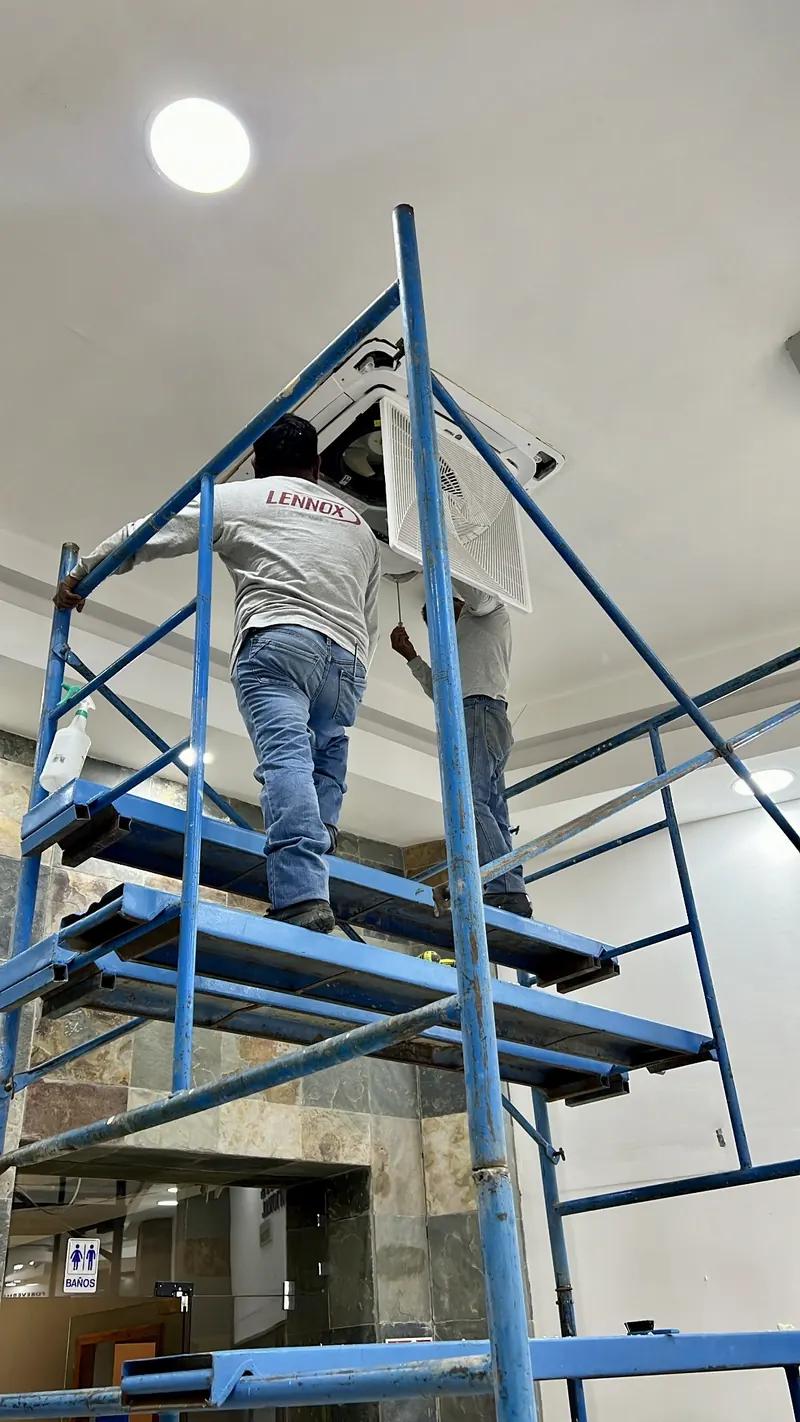 Técnicos de Grupo Green Air instalando un equipo en plafón a doble altura sobre andamio